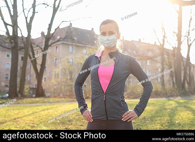 Fit woman during health crisis exercising outdoors wearing mask on a meadow