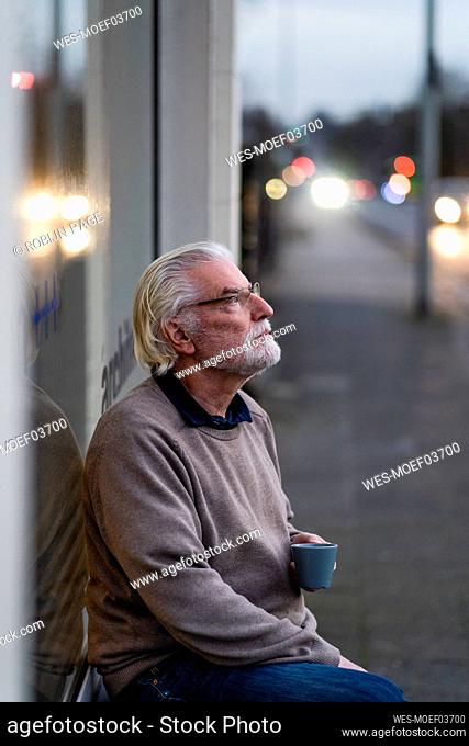 Thoughtful senior man sitting outside cafe at street