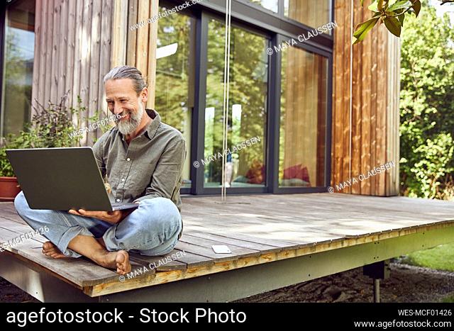 Bearded mature man using laptop while sitting outside tiny house