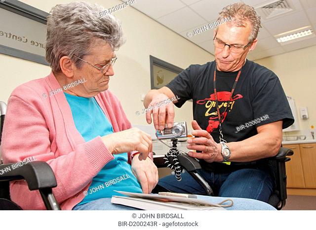 Wheelchair user with Parkinson's disease and osteoporosis in the spine with Day Service Officer in photography class at a resource for people with physical and...