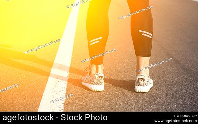 Closeup of male in running shoes going for run on road at sunrise or sunset. Man's legs in jogging shoes on road near park. Toned