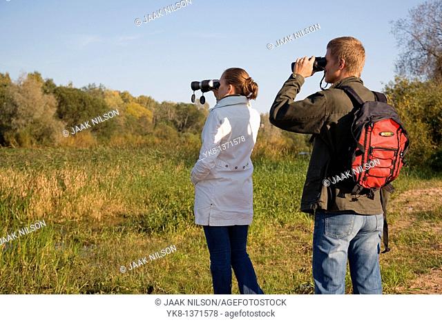 Young couple birdwatching with binoculars by river water