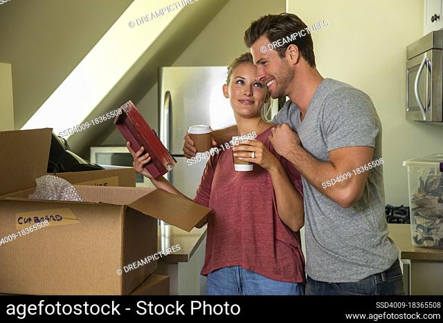 Young couple with coffee unpacking boxes after moving in to new home