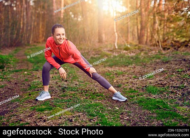 Full length portrait of a happy fit young woman doing stretching exercises for legs and arms during outdoor workout in the forest in Springtime
