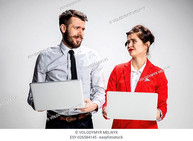 The young businessman and businesswoman with laptops communicating on gray background. The concept of relationship of colleagues