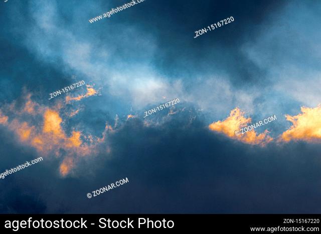 Fluffy clouds illuminated by disappearing rays at sunset and dark thunderclouds floating across sky to change season weather