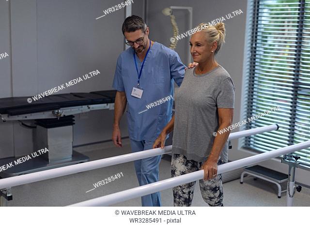 Front view of Caucasian male physiotherapist helping Caucasian female amputee patient walk with parallel bars in the hospital