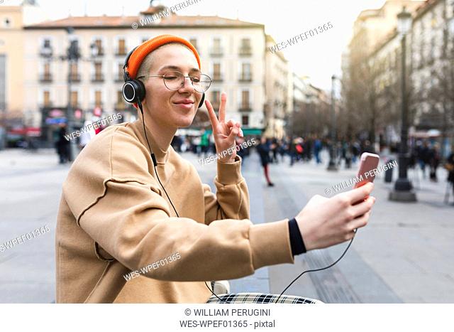 Young woman taking a selfie while listening to music and making peace gesture with her hand