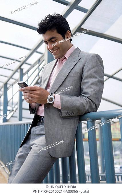 Businessman standing on a footbridge and text messaging on a mobile phone, Gurgaon, Haryana, India