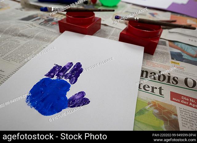 02 February 2022, Hessen, Darmstadt: A hand made of finger paints on a sheet of paper lies on a table in a daycare center