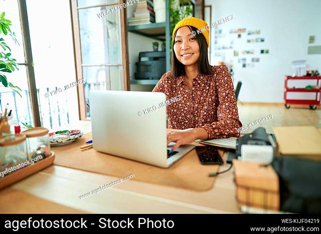 Female professional wearing knit hat sitting with laptop at workplace