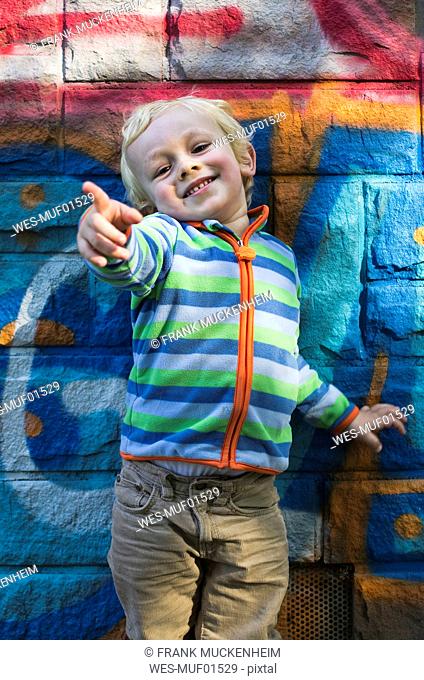 Portrait of smiling little boy standing in front of colourful wall pointing on something