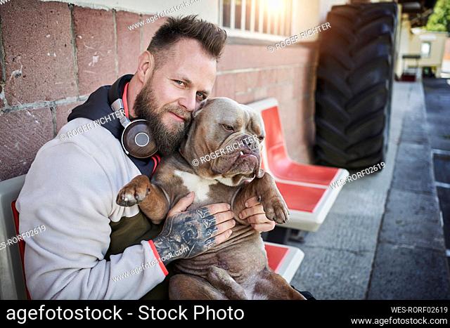 Male fitness instructor embracing bulldog outside gym