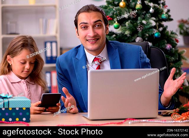 Young employee celebrating Christmas at workplace with his small daughter