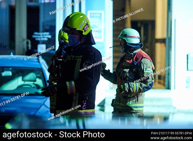 17 January 2021, Berlin: Three firefighters are standing in front of a house entrance. In the Muthesiusstraße in Steglitz a fire broke out in the 1st floor...
