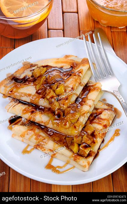 Breakfast pancakes on apples with caramel and chocolate and cup of tea
