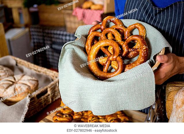 Mid section of staff holding wicker basket of pretzel breads at counter