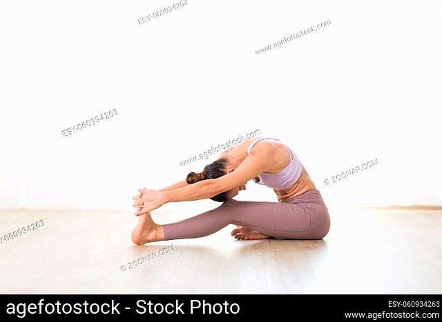 Portrait of gorgeous active sporty young woman practicing yoga in studio. Beautiful girl practice Janushiransa with Paschimotthanasana