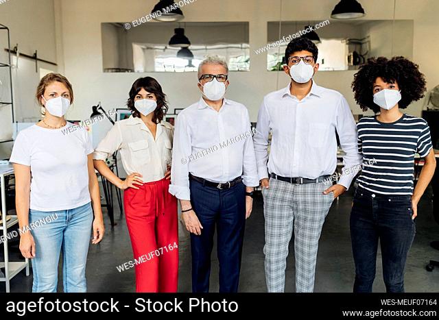 Coworkers wearing protective face mask standing together in office