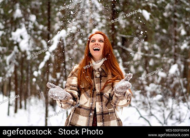 Cheerful woman playing in snow at winter forest
