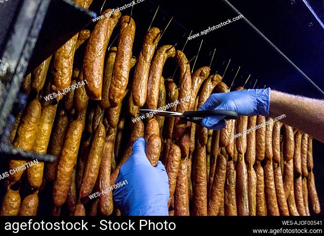 Hand of manual worker cutting sausages at food factory