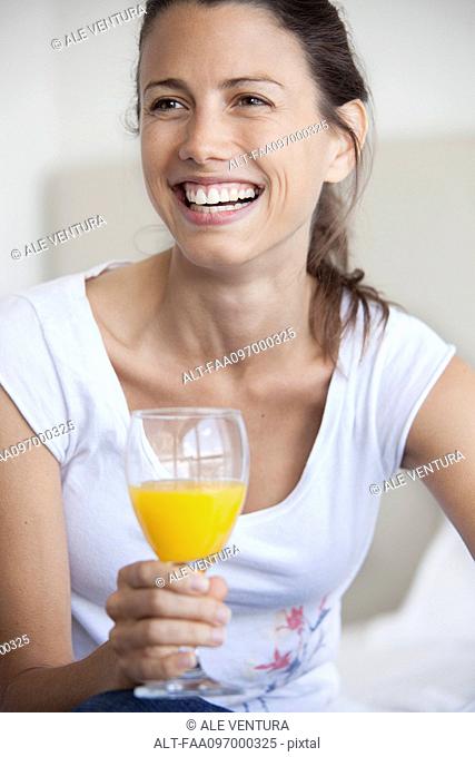 Woman holding glass of juice, smiling cheerfully