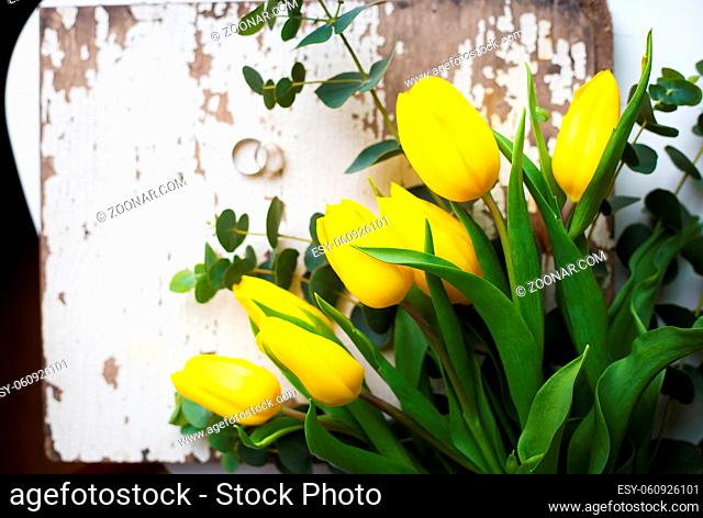 Beautiful wedding rings with yellow tulips on old white table