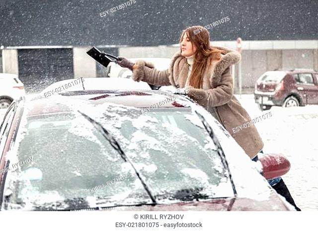 Young woman cleaning snow from car roof using brush
