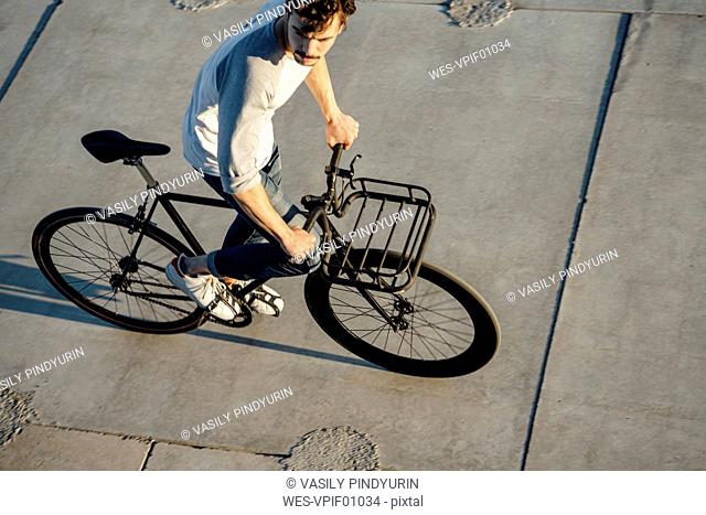 Young man riding commuter fixie bike on concrete slabs