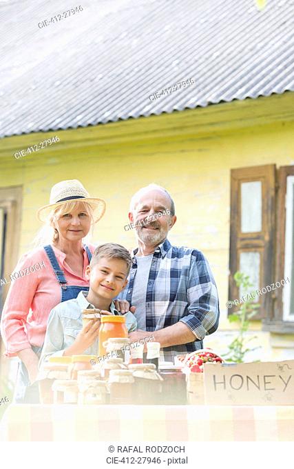 Portrait proud grandparents and grandson selling honey at farmer’s market stall