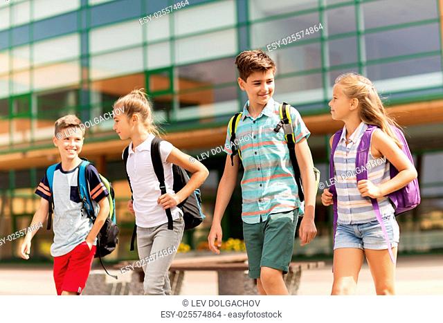 primary education, friendship, childhood, communication and people concept - group of happy elementary school students with backpacks walking and talking...