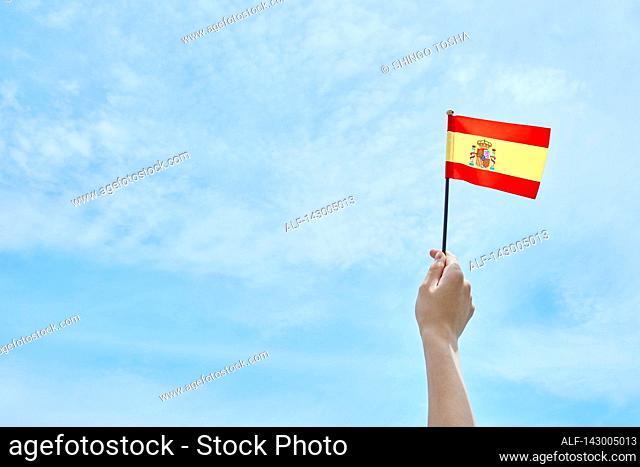 Hand holding flag against blue sky