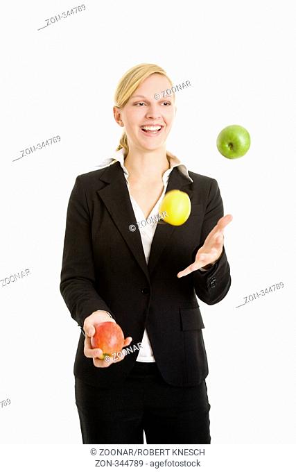 Blonde Frau im Jackett jongliert lachend mit drei Äpfeln