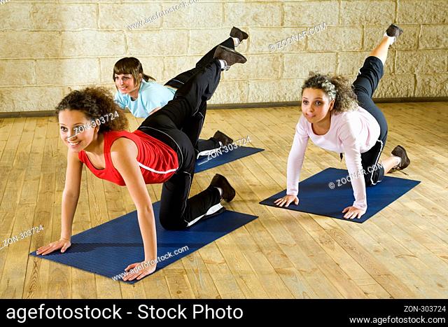 A group of women making stretching exercise on yoga mat. They're smiling and looking somewhere. Focus on the woman in pink shirt. Front view