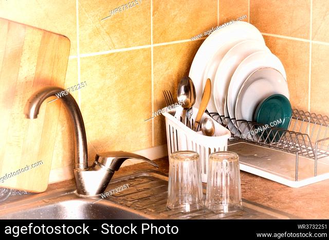 Washed plates, cutlery and glasses, drying in their racks close to the sink in the kitchen