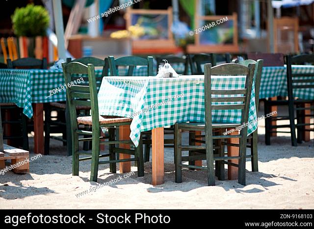 Empty Wooden Tables and Chairs with Green and White Checkered Tablecloths on Sunny Outdoor Restaurant Patio