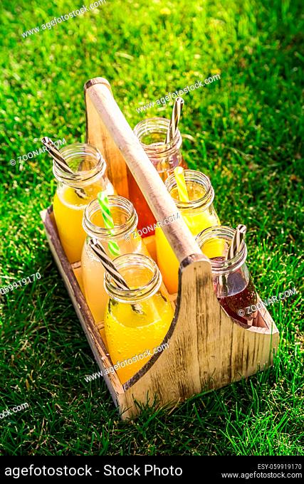 Assortment of lemonade and ice tea in bottles in wooden rack in the grass