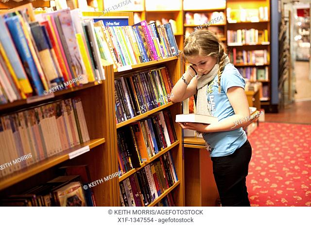 A twelve year old teenage girl reading in a bookshop, UK