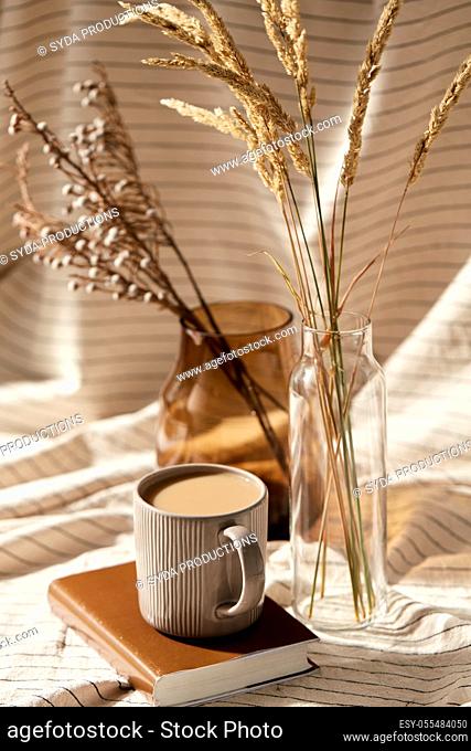 cup of coffee on book and dried flowers in vases