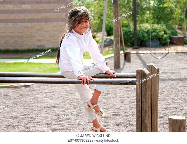 Little girl sitting on top of parallel bars at playground