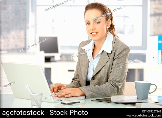Attractive young businesswoman working on laptop in bright office