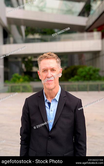 Portrait of mature businessman in suit in the city with nature outdoors