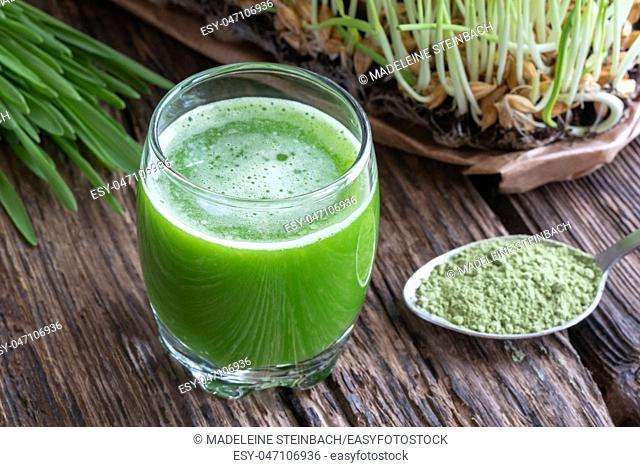 A glass of barley grass juice, with fresh and powdered plant in the background