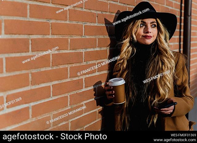 Woman in hat holding coffee cup while looking away during sunny day