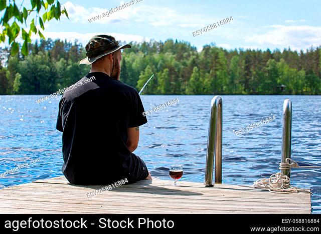 Mature man fishing from wooden pier near cottage on lake in Finland at summer