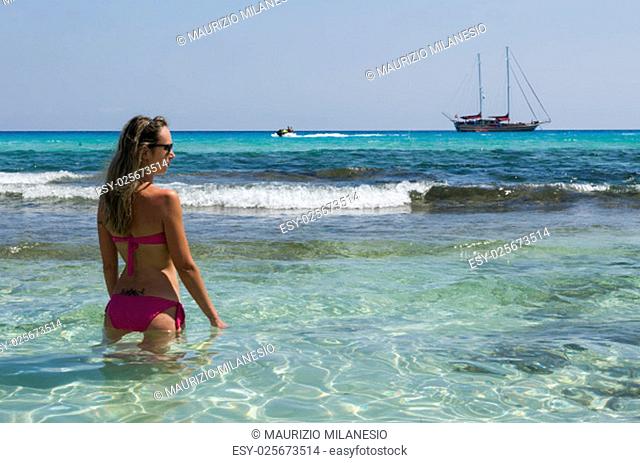 Blond girl looks sailing ship sea blue and green to the beach
