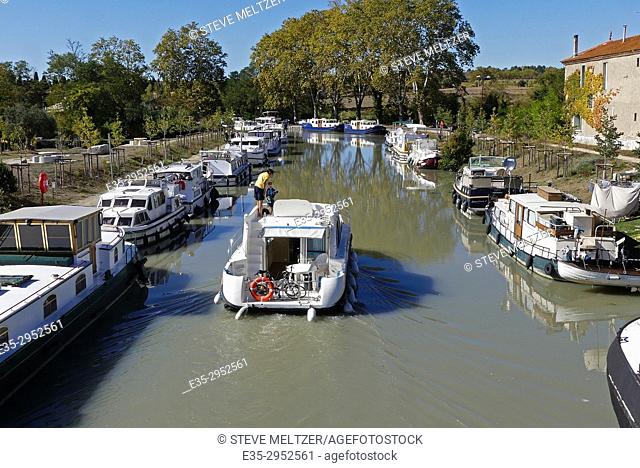 A father and son piloting a boat down the Canal du Midi at Capestang, France