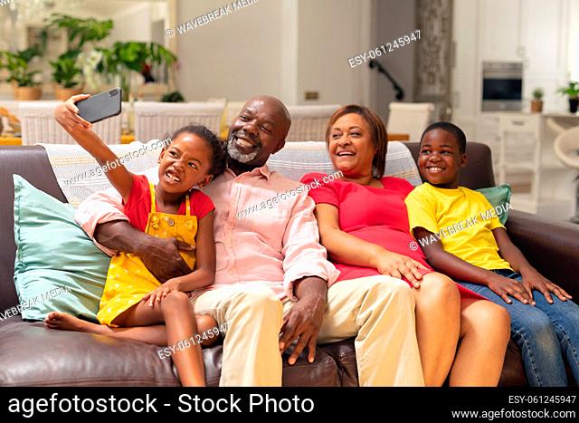 African american girl taking selfie with brother and grandparents while sitting on sofa at home