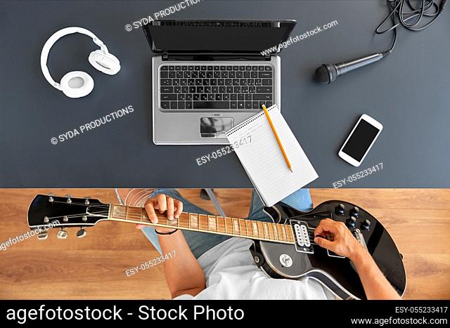 young man with laptop playing guitar at table