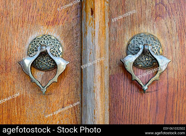 Closeup of two antique copper ornate door knockers over an aged wooden ornate door, Fatih Mosque, Istanbul, Turkey